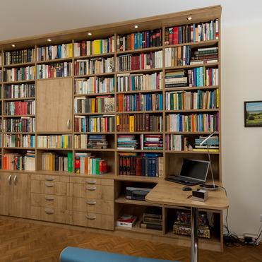 Maßgefertigtes Bücherregal von ASADA – Kundendesign im Wohnraum Großes Bücherregal nach Maß von ASADA mit integrierter Beleuchtung, Holzfronten, Schränken, Schubladen und Schreibtisch in einem gemütlichen Wohnraum mit vielen Büchern und persönlicher Einrichtung.