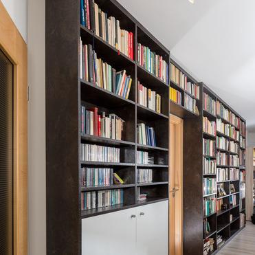 Dunkles Bücherregal nach Maß von ASADA – Platz für Bücher und Medien Dunkles maßgefertigtes Bücherregal mit integrierten Schränken und offenen Regalfächern, das entlang eines Flurs verläuft. Ideal für die Aufbewahrung von Büchern, CDs und persönlichen Sammlungen.