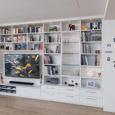 Maßgefertigte Wohnwand von ASADA – Kombination aus Regal und TV-Bereich Stilvolle weiße Wohnwand mit offenen Regalen, Schubladen und Glaselementen. Integrierter TV-Bereich und dekorative Beleuchtung schaffen eine funktionale und moderne Wohnraumlösung.