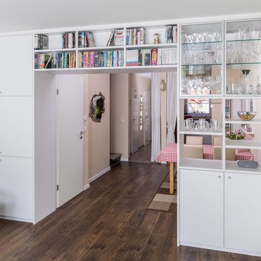 Maßgefertigte Durchgangsregalwand von ASADA – Raumtrennung mit Stil Maßgefertigte Regalwand mit integriertem Glaselement zur Präsentation von Gläsern. Das Regal schafft eine elegante Raumtrennung zwischen Wohnzimmer und Essbereich und bietet zusätzlichen Stauraum.