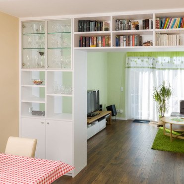 Maßgefertigte Regalwand von ASADA – Stilvolle Raumtrennung zwischen Ess- und Wohnbereich Weiße Regalwand mit offenen und geschlossenen Fächern sowie Glaselementen. Die maßgefertigte Lösung dient als elegante Raumtrennung und bietet Platz für Bücher, Gläser und Dekorationen.
