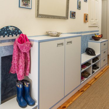 Eine Garderobe nach Maß mit Schuhregalen, Stauraum, Kleiderhaken und Ablagen in einem hellen Flur. An der Wand hängen Bilder und ein großer Spiegel.