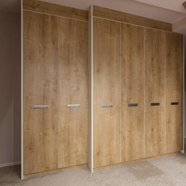 Ein großer Eckschrank mit Türen in Holzoptik, gestaltet als Kleiderschrank nach Maß in einem Raum mit Teppichboden.