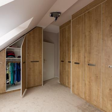 Ein offener Kleiderschrank nach Maß unter einer Dachschräge mit Kleidung und Holztüren in einem Dachgeschosszimmer.
