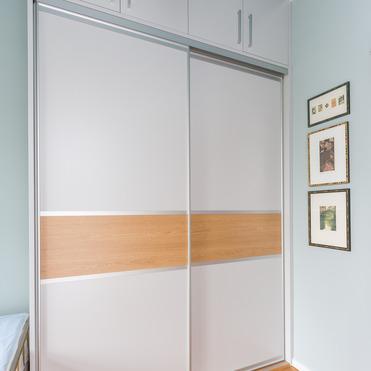 Moderner Kleiderschrank nach Maß mit weißen Türen und einer horizontalen Holzleiste, neben gerahmten Bildern an einer hellblauen Wand.