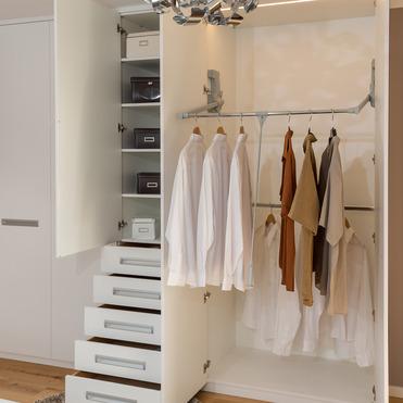 Ein geöffneter, maßgefertigter Kleiderschrank zeigt Hemden auf Bügeln und Schubladen, in einem eleganten Raum mit Holzboden.