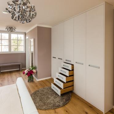 Elegantes Zimmer mit einem großen, maßgeschneiderten Kleiderschrank neben einem Bett und einem modernen Kronleuchter.