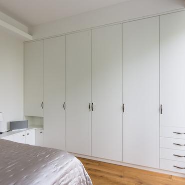 Geräumiges Schlafzimmer mit einem wandfüllenden, maßgeschneiderten Kleiderschrank und Schubladen in Weiß.