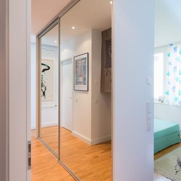 Heller Flur mit Parkettboden und einem hohen, maßgeschneiderten Kleiderschrank, dessen Türen als Spiegel dienen.