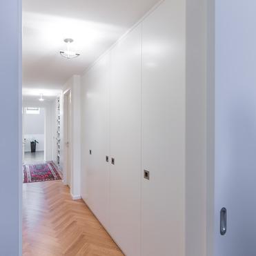 Moderner, langer Flur mit Parkettboden und nahtlos integriertem, weißem Kleiderschrank nach Maß.
