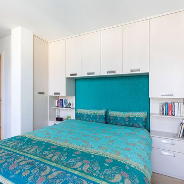 Ein Schlafzimmer mit einem großen Bett vor einem maßgeschneiderten Kleiderschrank, der sich über das Kopfende erstreckt.