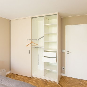 Ein teilweise geöffneter Eckschrank nach Maß mit Regalen und Kleiderstange in einem eleganten Schlafzimmer.