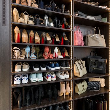 Nahaufnahme eines dunklen Holzschuhschranks, der eine Vielzahl von Schuhen und einigen Designerhandtaschen ordentlich präsentiert. Eine breite Palette von Stilen und Farben ist sichtbar.