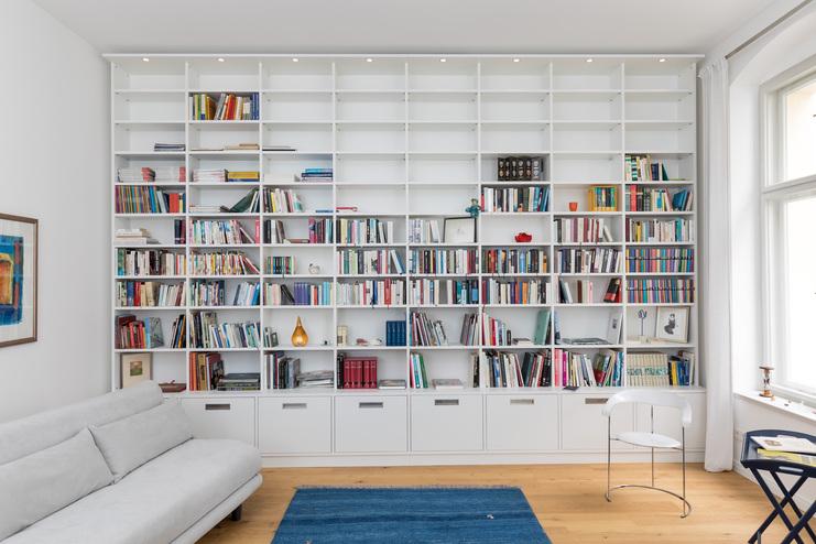 Ein großes, weißes Bücherregal nach Maß mit zahlreichen Fächern, gefüllt mit Büchern, integriert über weißen Schubladen.