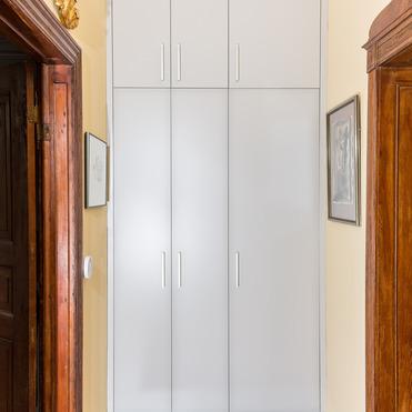 Ein schlichter, moderner, weißer Schrank kontrastiert mit dem traditionellen Holzdekor und einer kunstvollen Skulptur in einem eleganten Eingangsbereich.