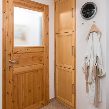 Ein gemütlicher Eingangsbereich mit naturbelassenen Holztüren und einem abgestimmten Schrank, ergänzt durch eine hängende Uhr und ein Handtuch an einem Haken an der Wand.