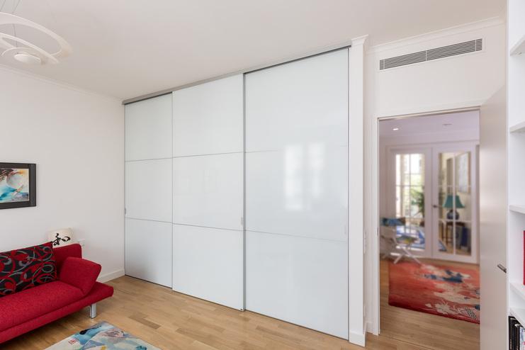 Große weiße Schiebetüren nach Maß im modernen Wohnzimmer mit Holzboden und rotem Sofa.