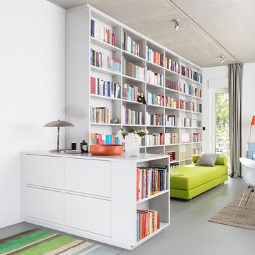 Helles und farbenfrohes Wohnzimmer mit einem großen, weißen Sideboard nach Maß, umfangreichen Bücherregalen und einem grünen Sofa. Stilvolle und funktionale Einrichtung.