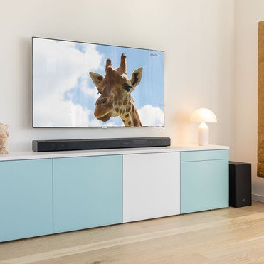 in modernes Wohnzimmer mit einem pastellfarbenen Sideboard, auf dem eine Figur und eine Tischlampe stehen. Ein Flachbildfernseher an der Wand zeigt das Bild einer Giraffe.