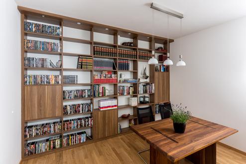 Ein elegantes Bücherregal aus Nussbaumholz füllt eine Wand eines modernen Arbeitszimmers. Das Regal bietet offene Fächer für Bücher und Dekoration sowie geschlossene Schrankelemente für zusätzlichen Stauraum.